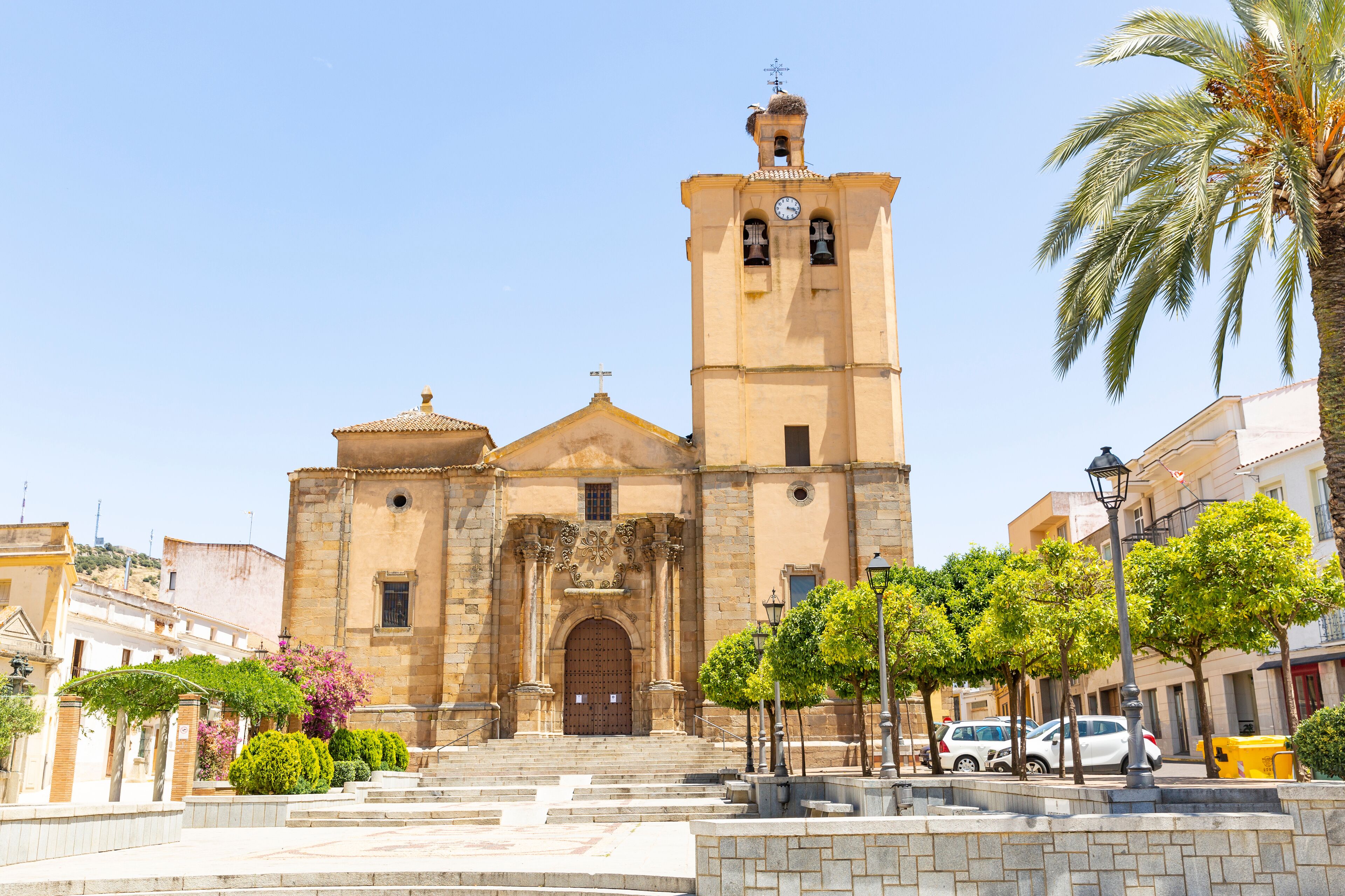 A historic church with a bell tower, steps leading up to the entrance, and surrounding trees and parked cars.