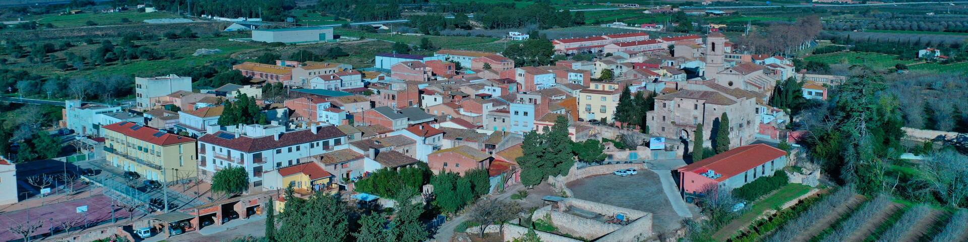 A town with colorful buildings, a church, and surrounding green fields and mountains.