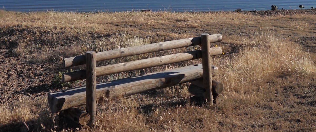 A wooden bench by a calm lake with a clear sky.