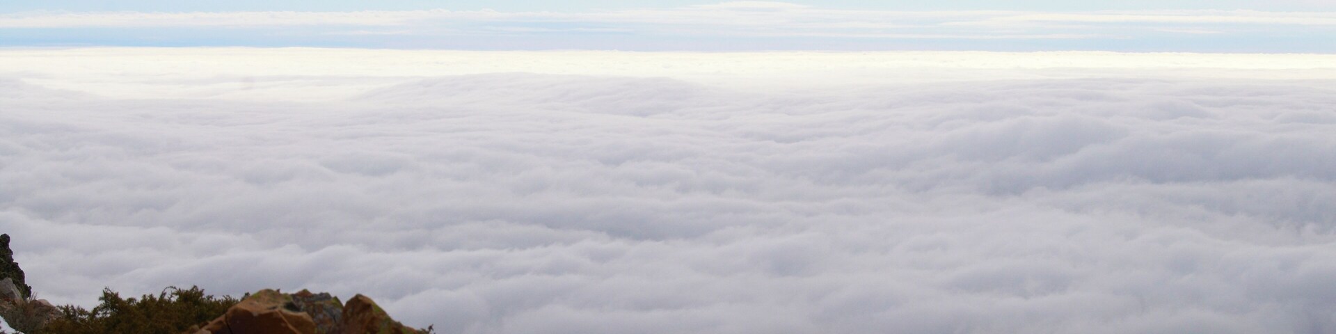 A mountain landscape with rocky outcrops and a sea of clouds below.