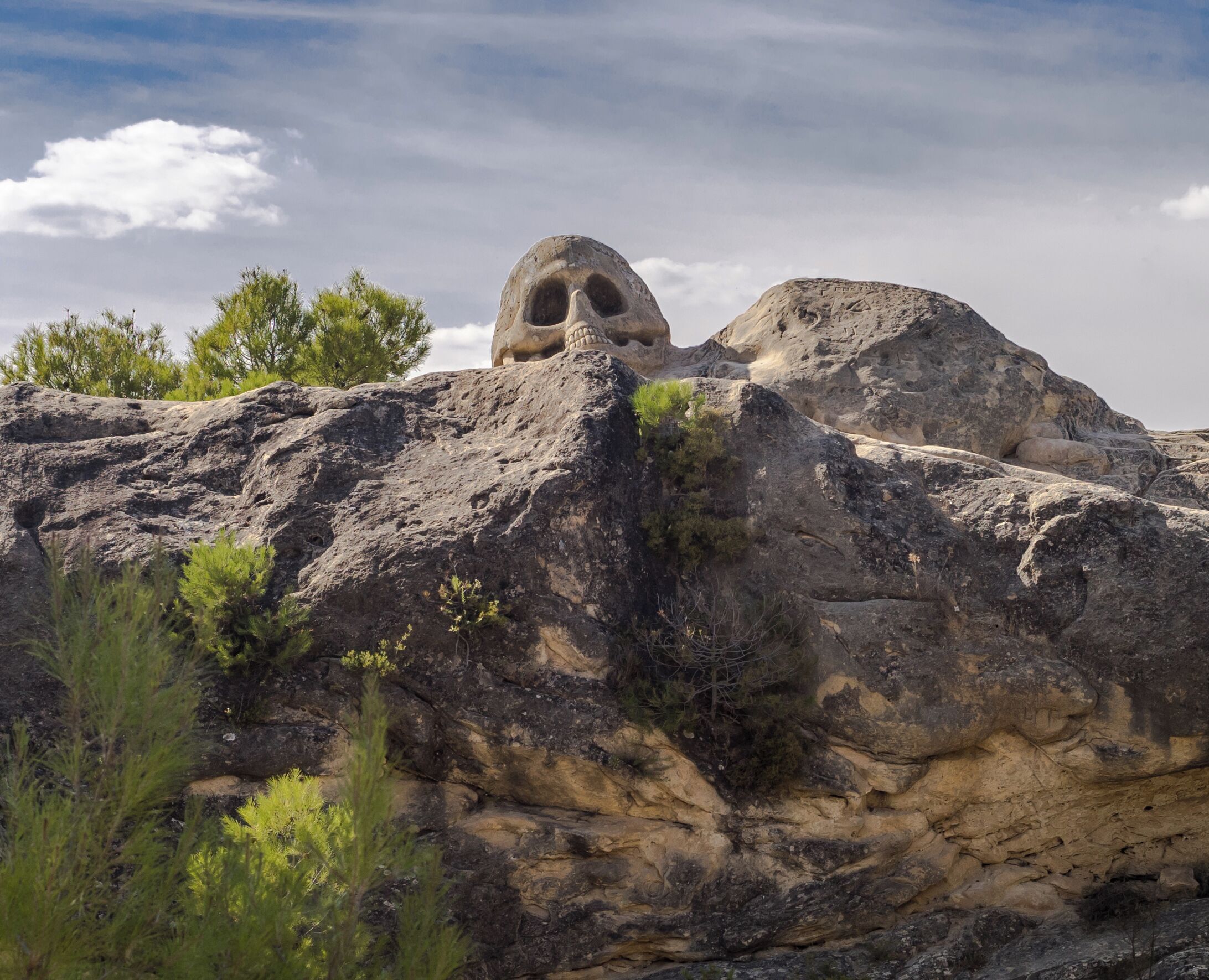A rocky landscape with large boulders and a prominent rock formation with a cave-like opening.