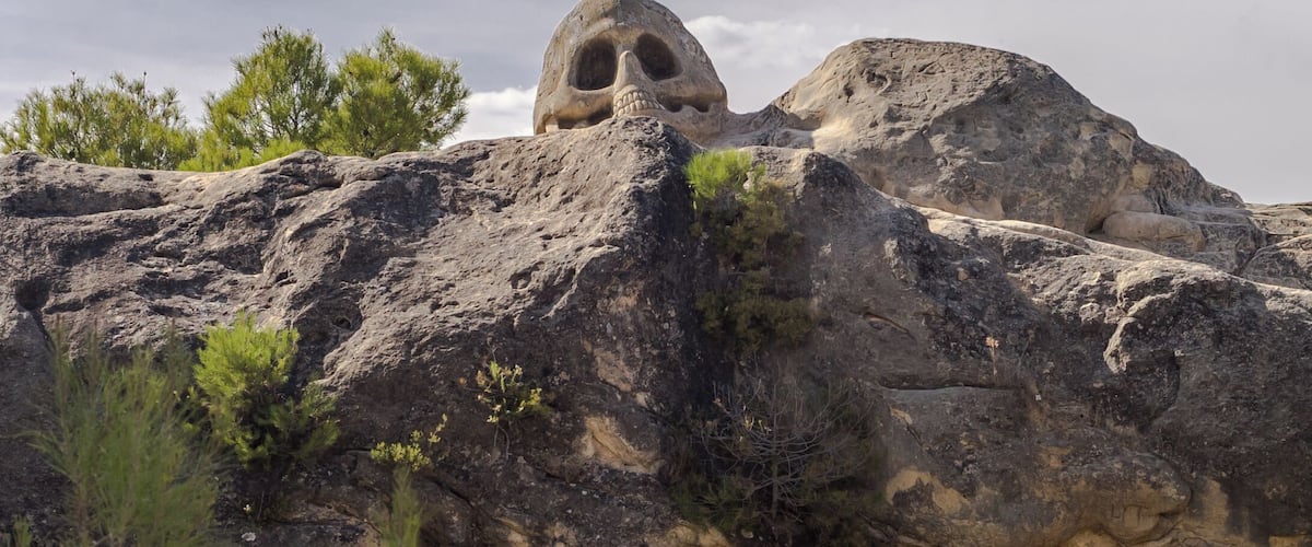 A rocky landscape with large boulders and a prominent rock formation with a cave-like opening.