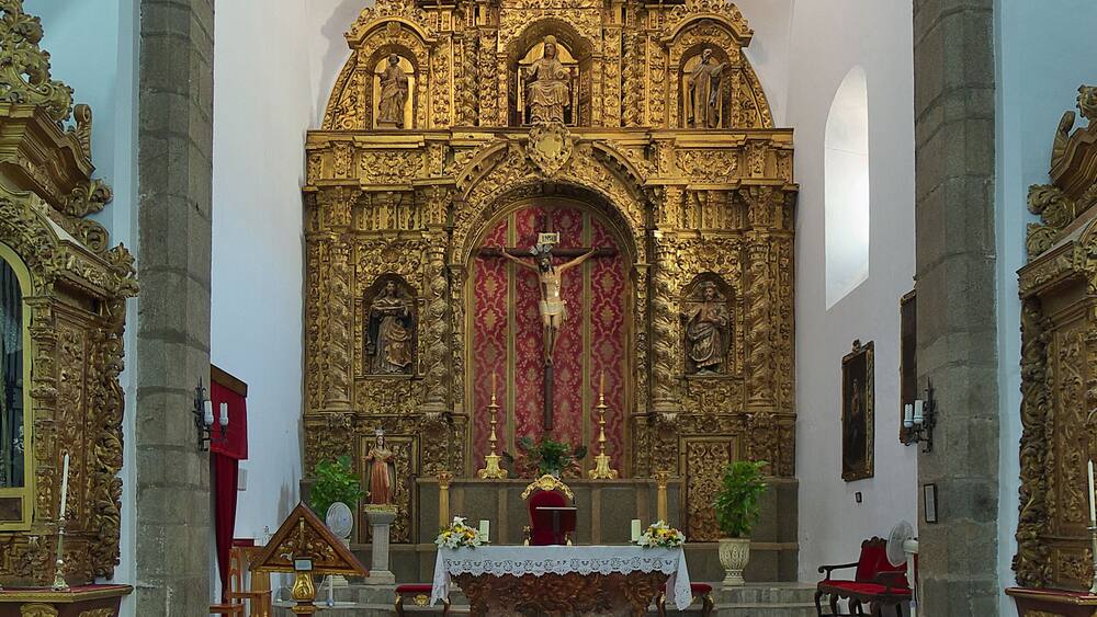 L’intérieur d’une église richement décorée, avec un tapis rouge menant à l’autel, agrémenté de motifs dorés et de statues.