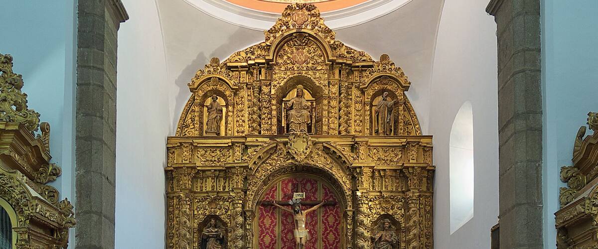 An ornate church interior with a red carpet leading to the altar, featuring golden decorations and statues.
