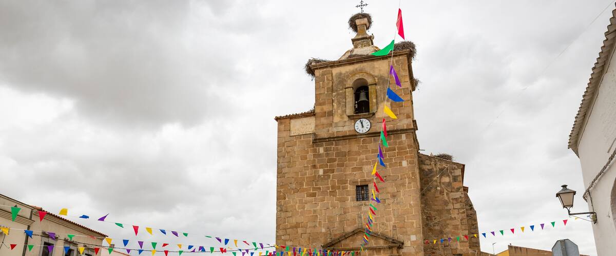 A historic church with a bell tower, surrounded by colorful flags and potted plants.