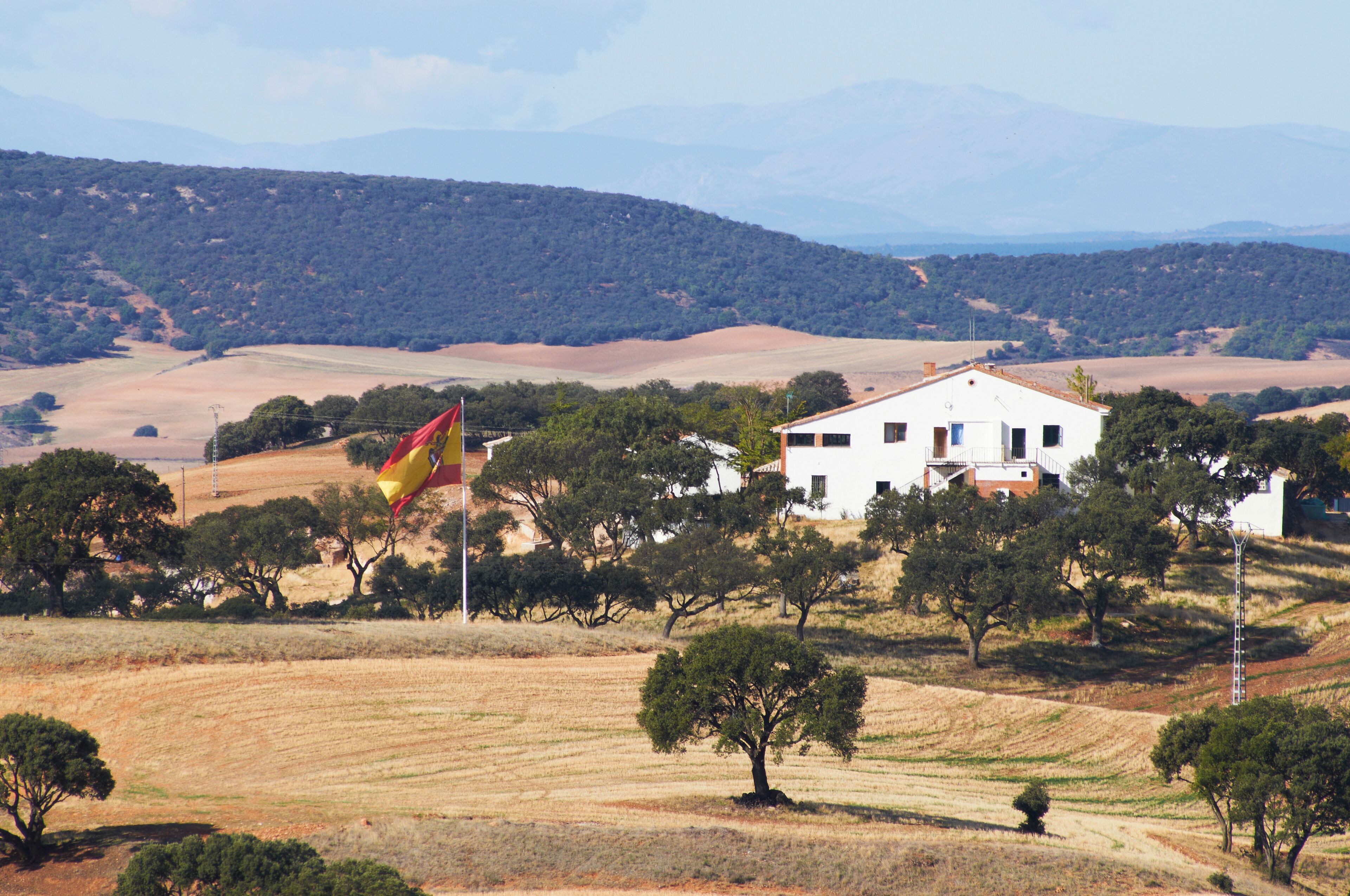 Una casa blanca rodeada de árboles y campos en un paisaje montañoso.