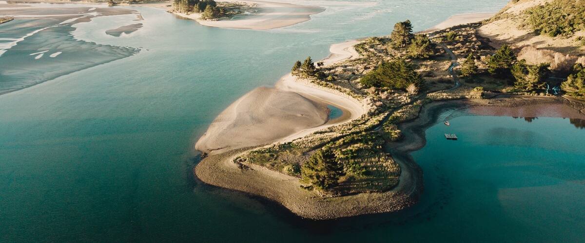 An aerial view of a coastal landscape with a large bay, sandy beaches, and a small island with trees.