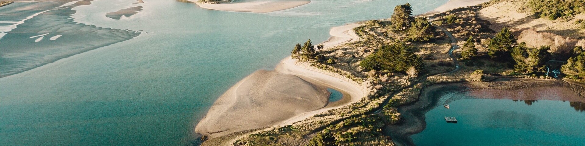 An aerial view of a coastal landscape with a large bay, sandy beaches, and a small island with trees.