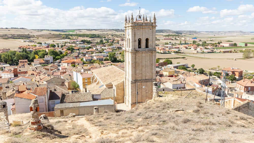 Une ville historique, reconnaissable à son imposante tour, entourée de maisons à étages et de champs.