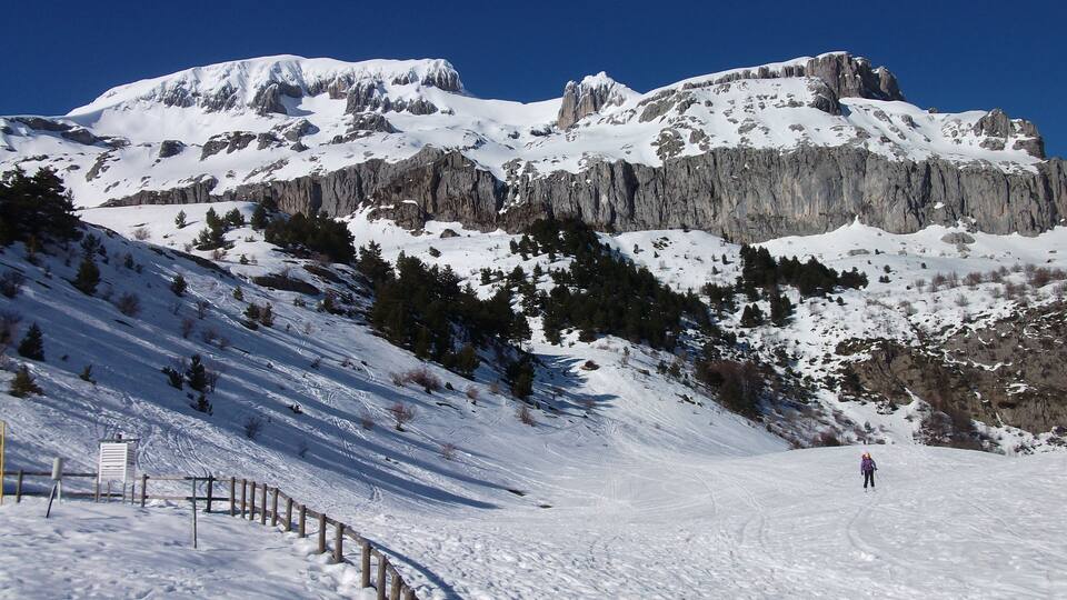 A snow-covered mountain with rocky cliffs and a skier.