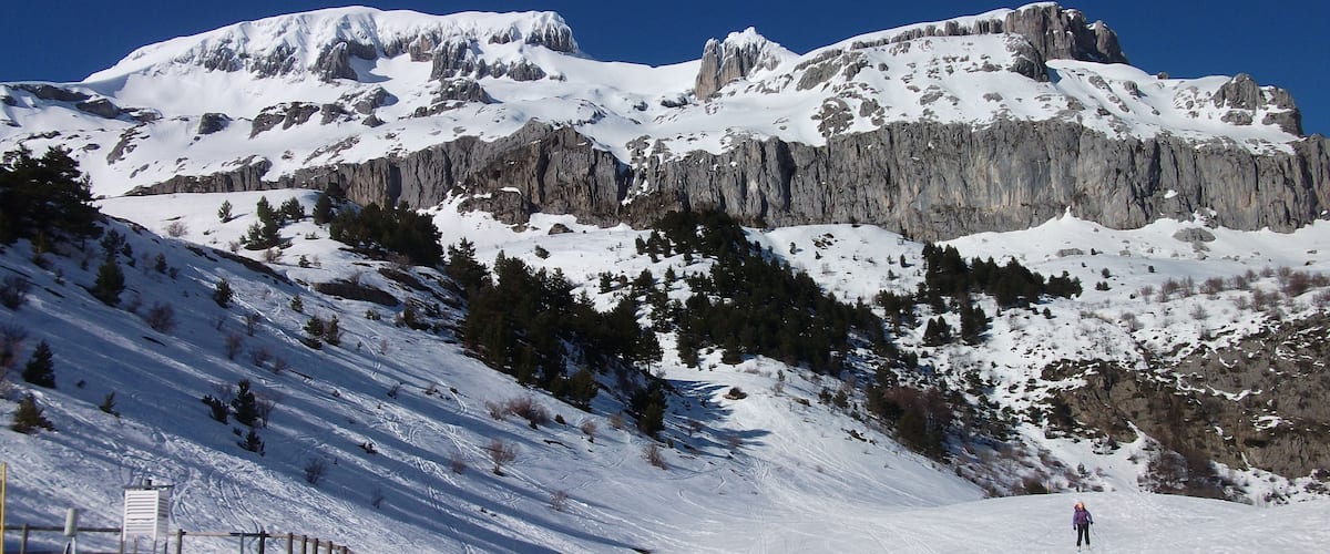 A snow-covered mountain with rocky cliffs and a skier.