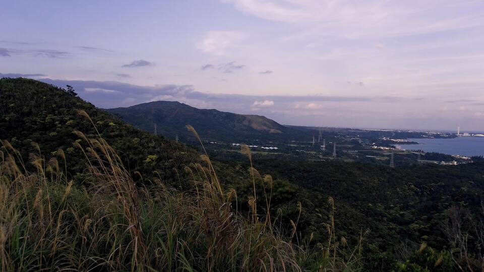 A coastal landscape with a hill, grass, and a distant view of a body of water.
