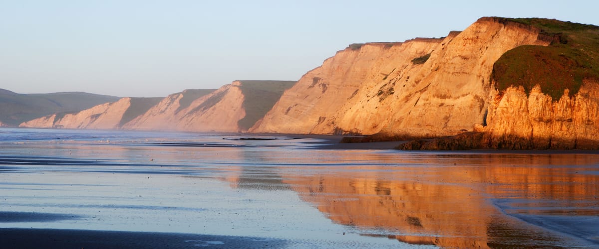 A coastal landscape with cliffs and a reflective wet surface.