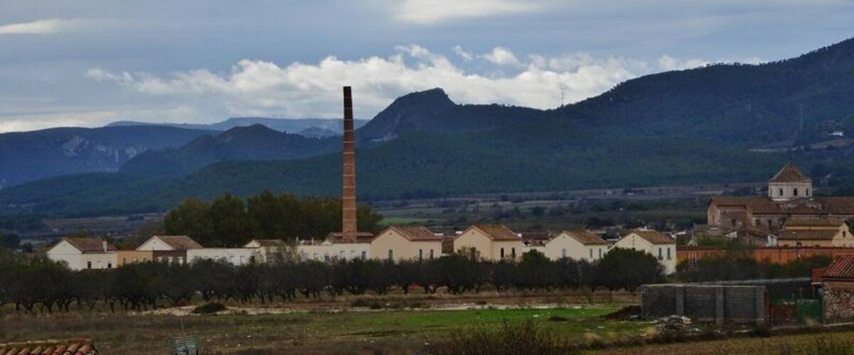 A town with a prominent chimney, houses, and mountains in the background.
