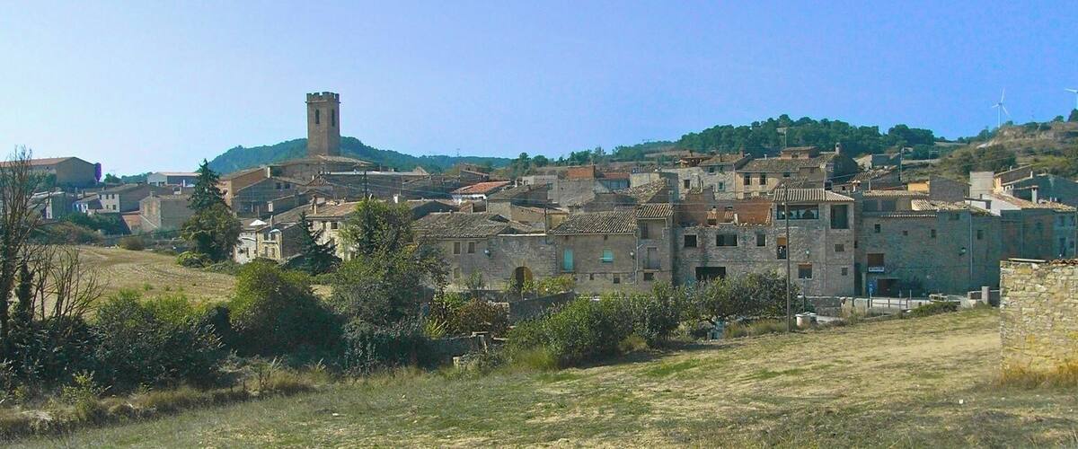 A historic town with stone buildings, a prominent tower, and wind turbines in the background.