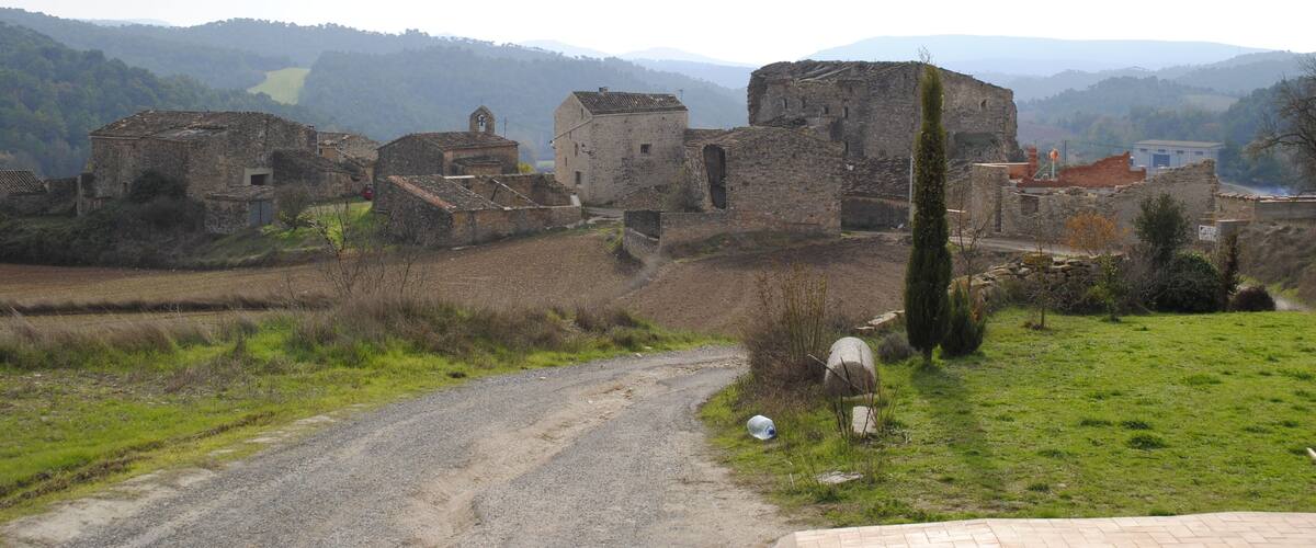 A rural landscape with old stone buildings, a dirt road, and rolling hills in the background.
