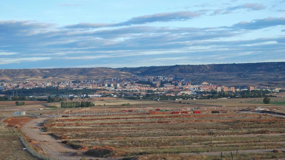 A cityscape with a large urban area in the background, surrounded by open fields and a hilly terrain.
