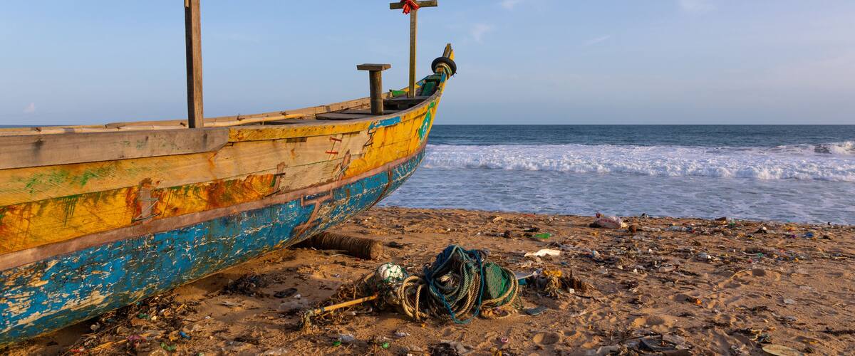 A weathered boat on a sandy beach with the ocean in the background.