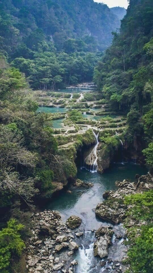 A river with a waterfall surrounded by lush greenery and rocky terrain.