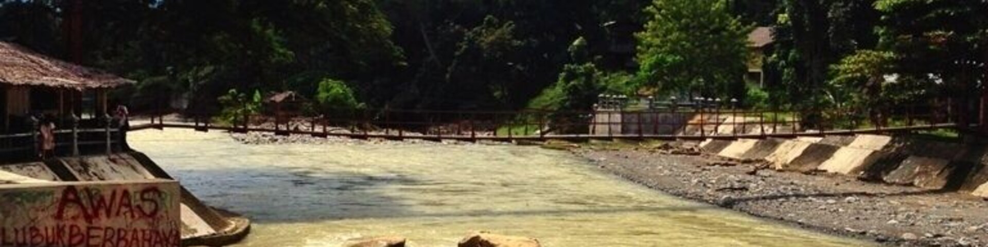 A river with rocks, a wooden structure, and a bridge.