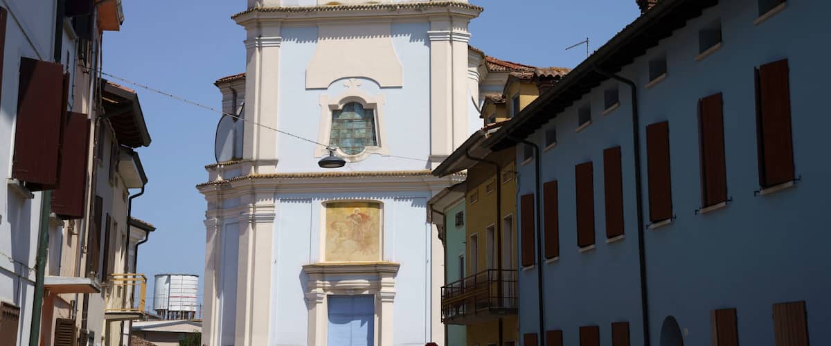 A church with a bell tower, a street with buildings, and a clear blue sky.