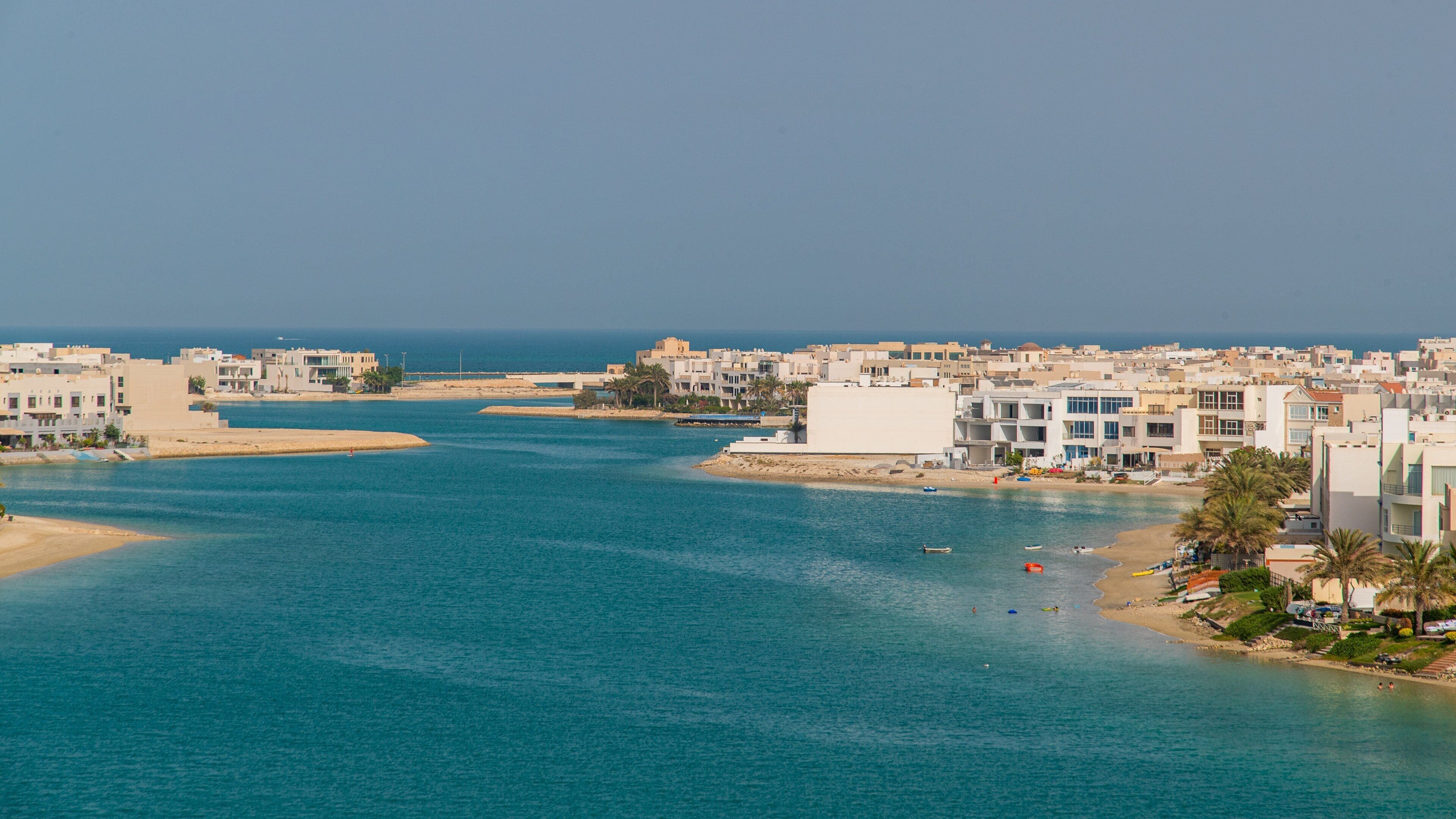 A coastal city with a clear blue sea, sandy beaches, and modern buildings.