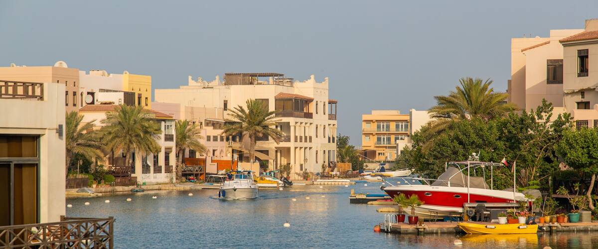 A marina with boats docked, surrounded by buildings and palm trees.