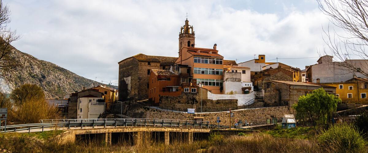 A historic town with a prominent church tower, a bridge, and buildings along a river.