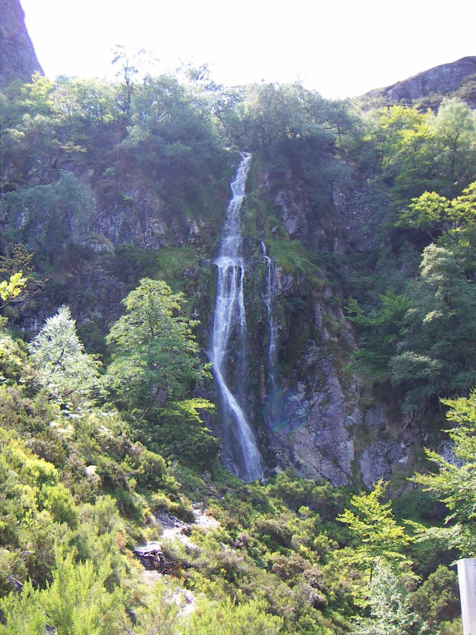 A waterfall cascading down a rocky cliff surrounded by lush greenery.