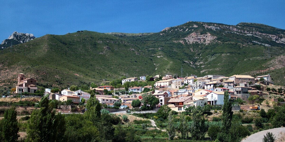A hillside village with buildings, greenery, and a mountain in the background.