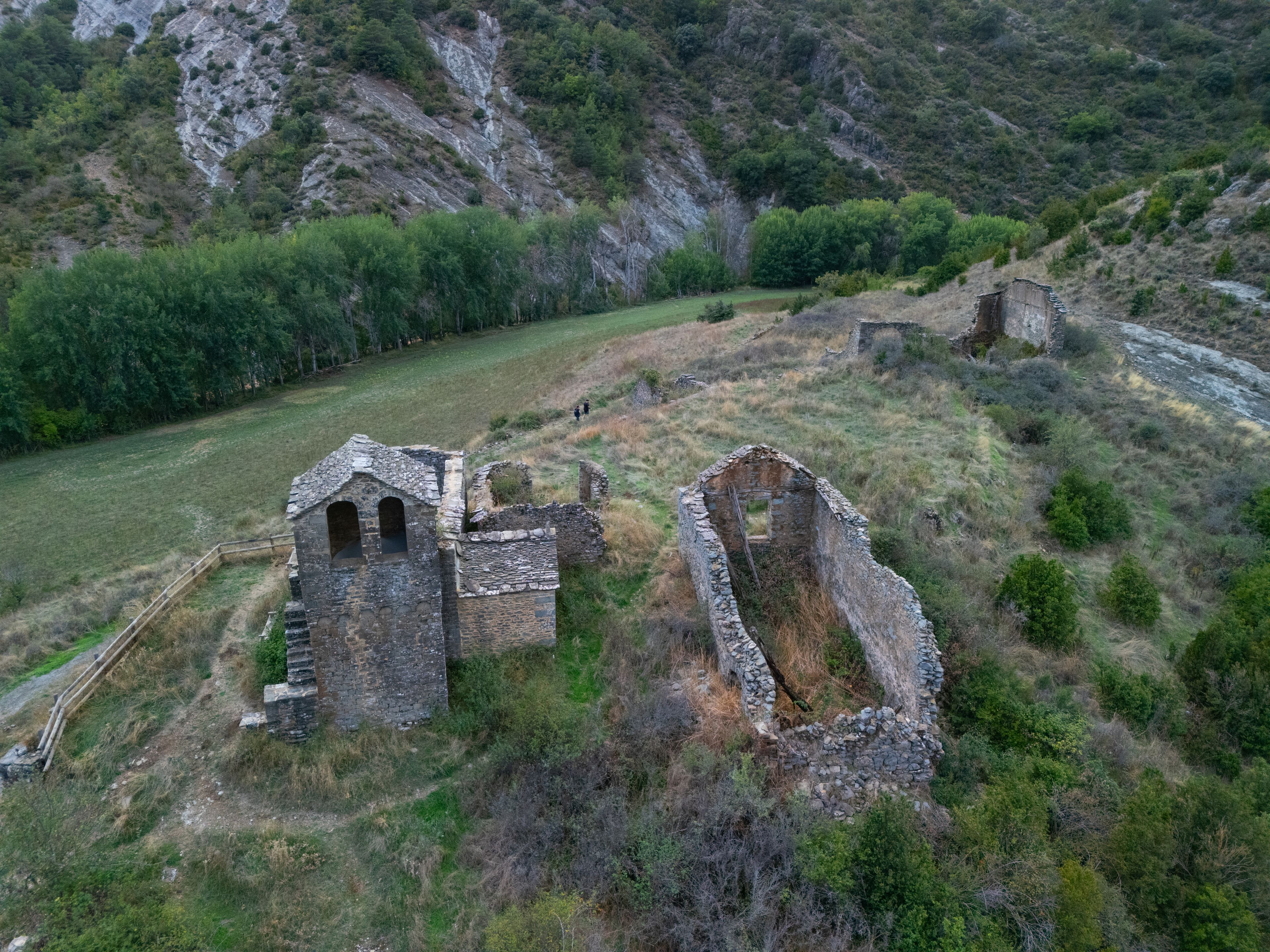 An aerial view of an ancient stone structure with ruins, surrounded by a mountainous landscape and dense greenery.