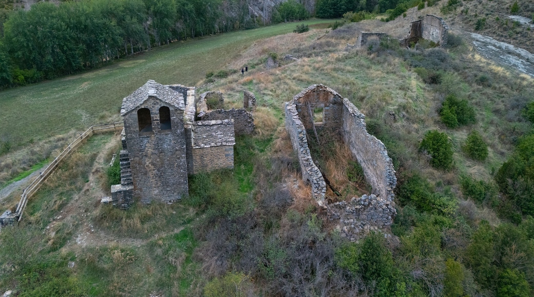 An aerial view of an ancient stone structure with ruins, surrounded by a mountainous landscape and dense greenery.