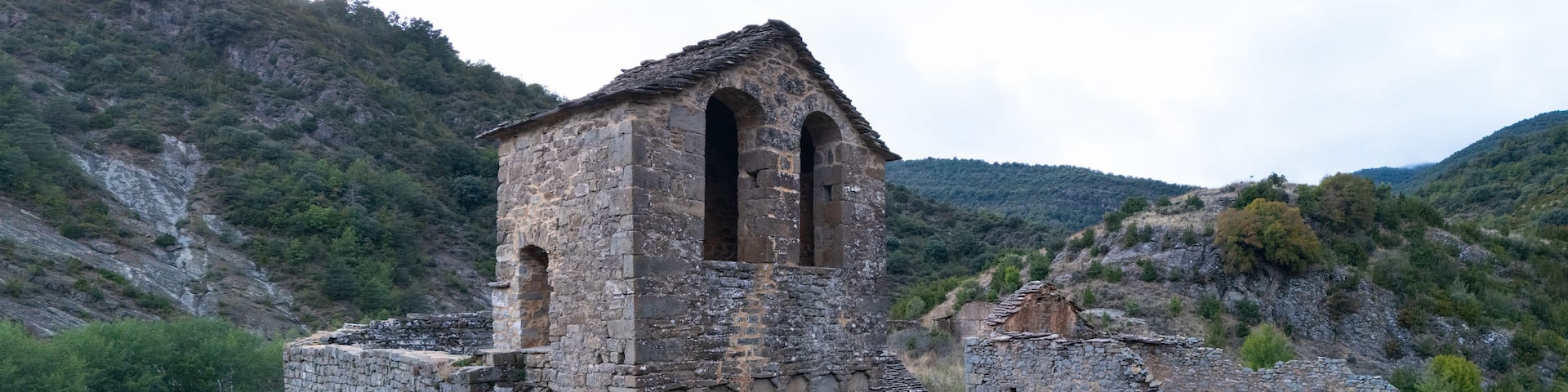 An ancient stone tower with arched openings, surrounded by rugged hills and sparse vegetation.