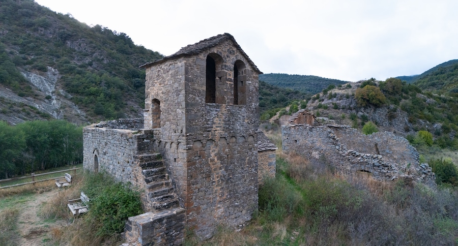 Una antigua torre de piedra con aberturas en arco, rodeada de colinas escarpadas y vegetación escasa.
