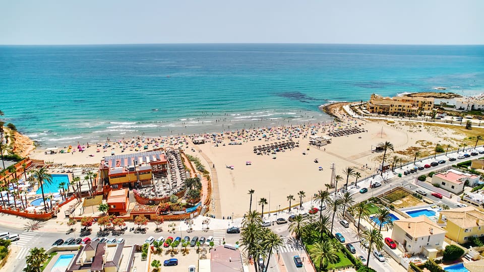 A coastal resort with a beach, swimming pools, and a large hotel.