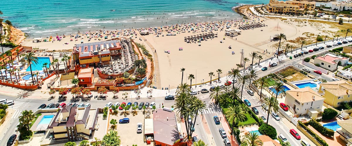 A coastal resort with a beach, swimming pools, and a large hotel.