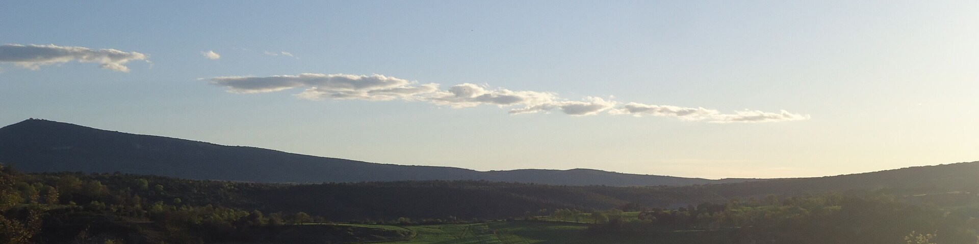 A lake surrounded by green fields and hills under a clear sky.