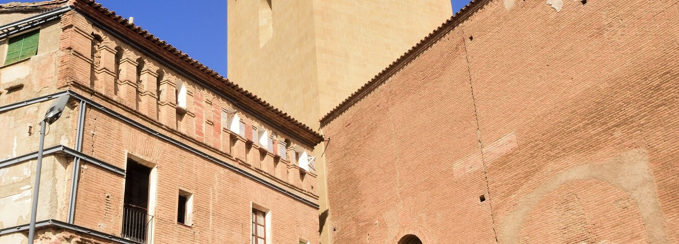 Um edifício histórico com uma torre alta, janelas em arco e uma porta grande.