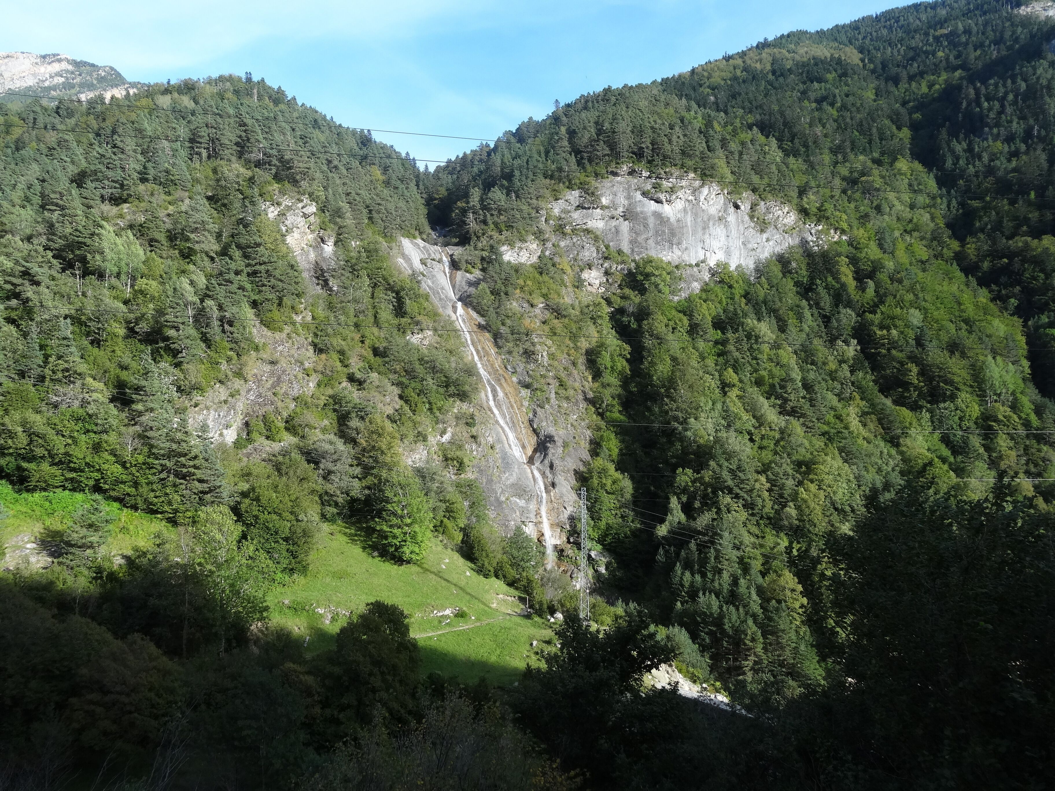 A mountainous landscape with a waterfall, dense forest, and a clear sky.