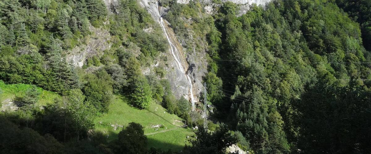 A mountainous landscape with a waterfall, dense forest, and a clear sky.