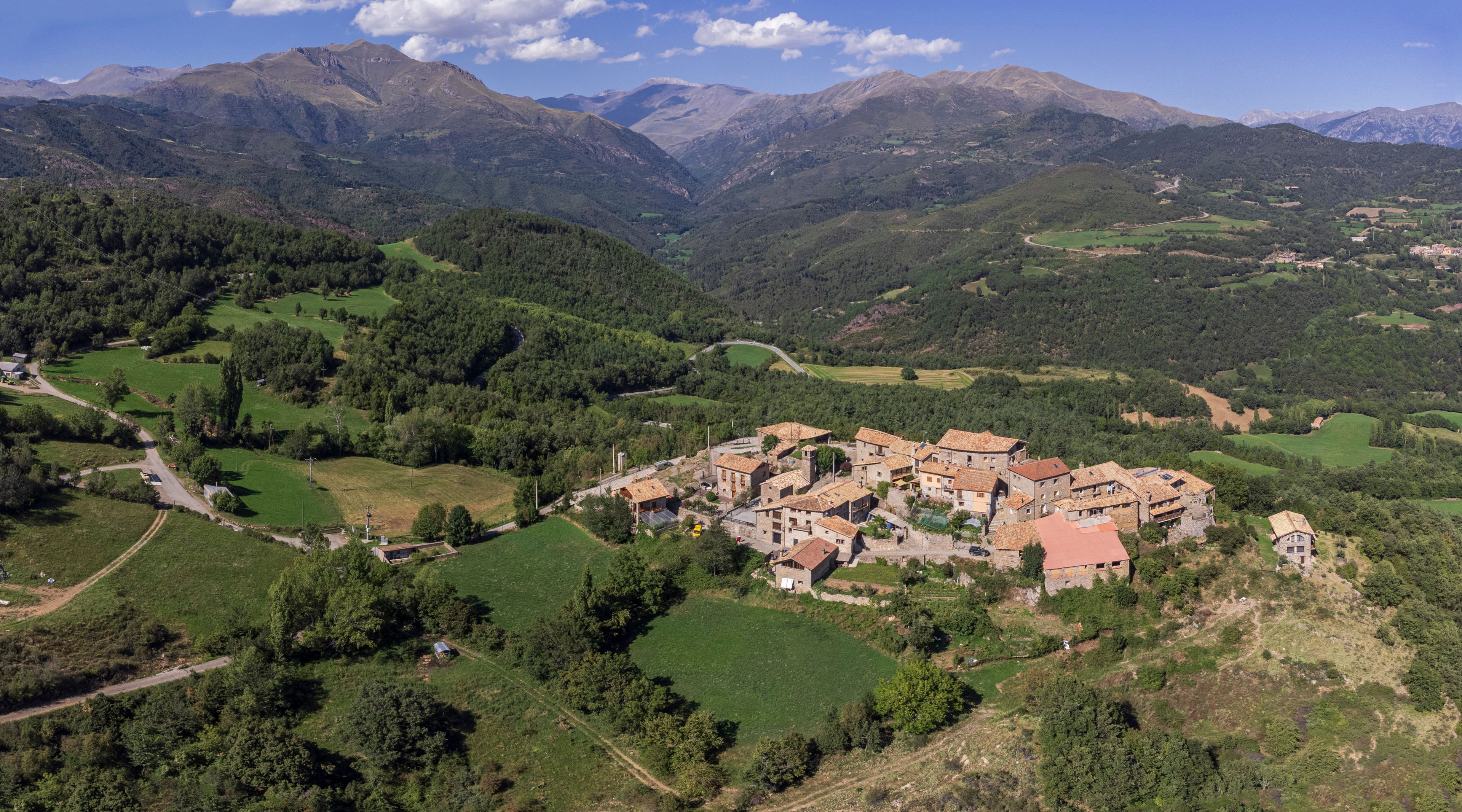 A mountainous landscape with a village nestled in a valley surrounded by lush greenery and distant peaks.