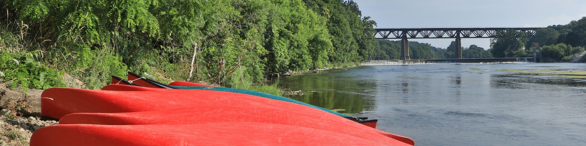 A red kayak on a rocky shore with a bridge in the background.