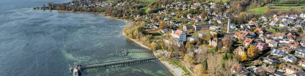 A coastal town with a pier extending into a calm lake, surrounded by hills and residential buildings.
