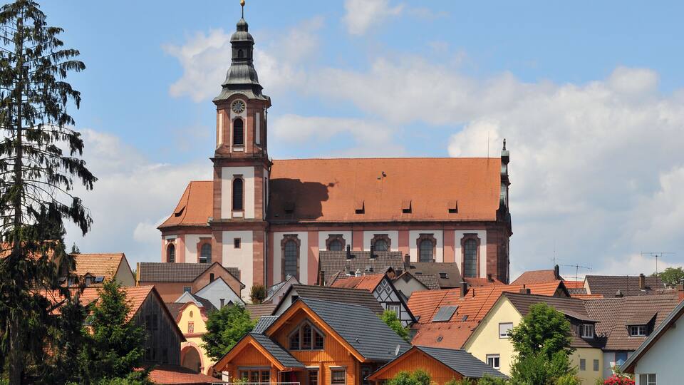 A church with a tall tower and red roof amidst residential buildings.
