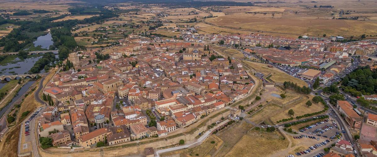 An aerial view of a historic town with a central square, surrounding buildings, and a river.