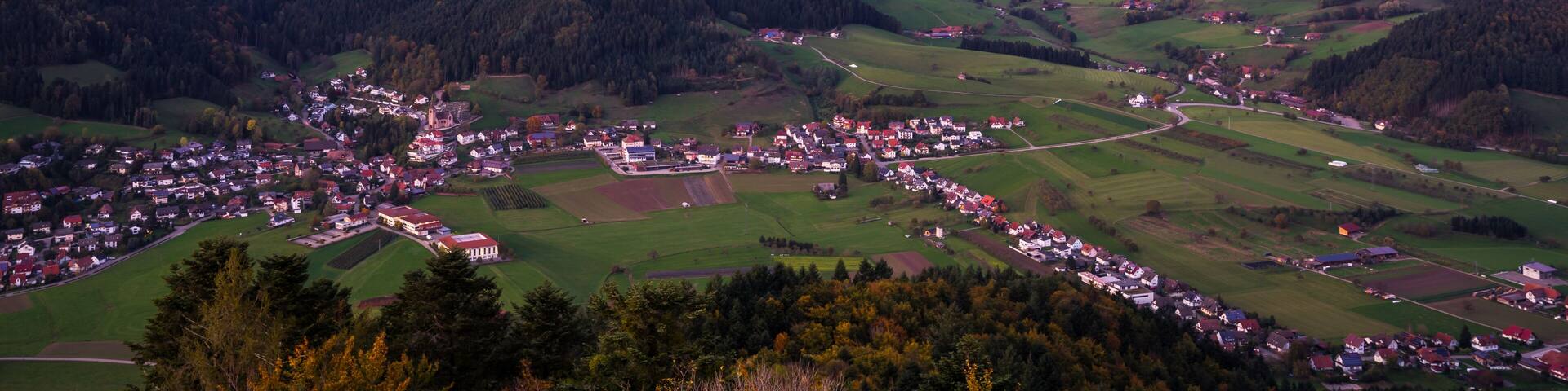 A rural landscape with rolling hills, a small village, and wind turbines in the distance.