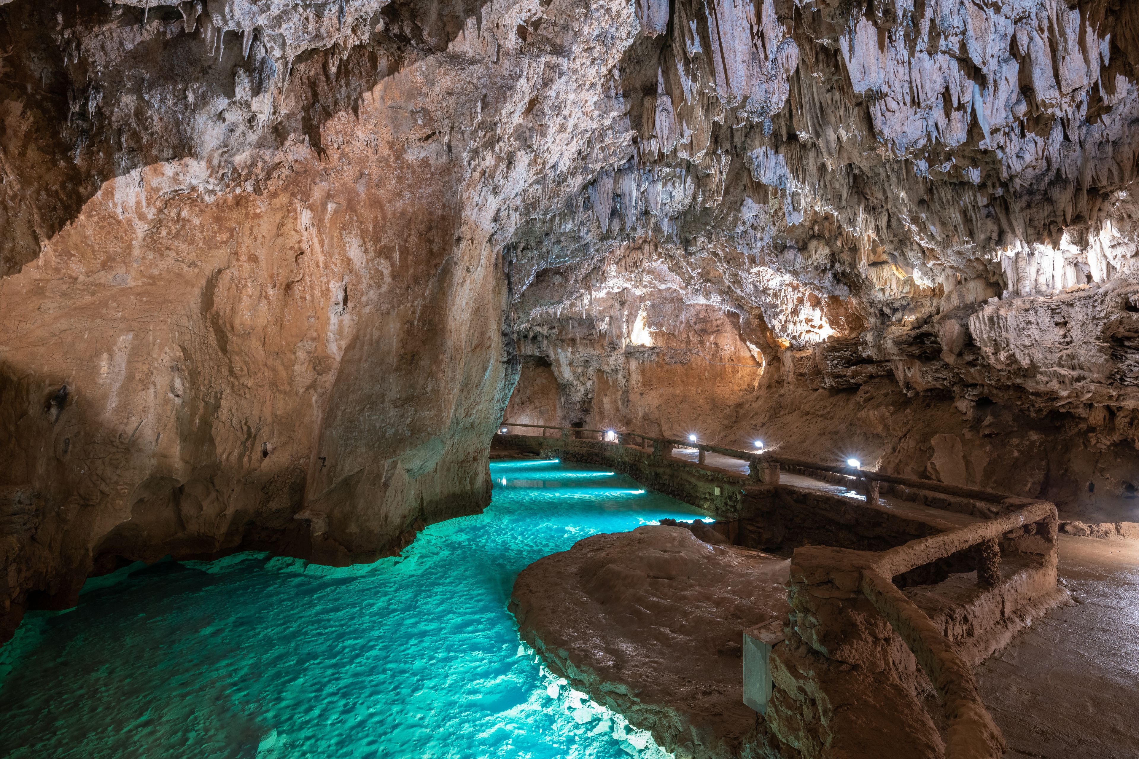 A cave with turquoise water, rocky formations, and a wooden walkway.