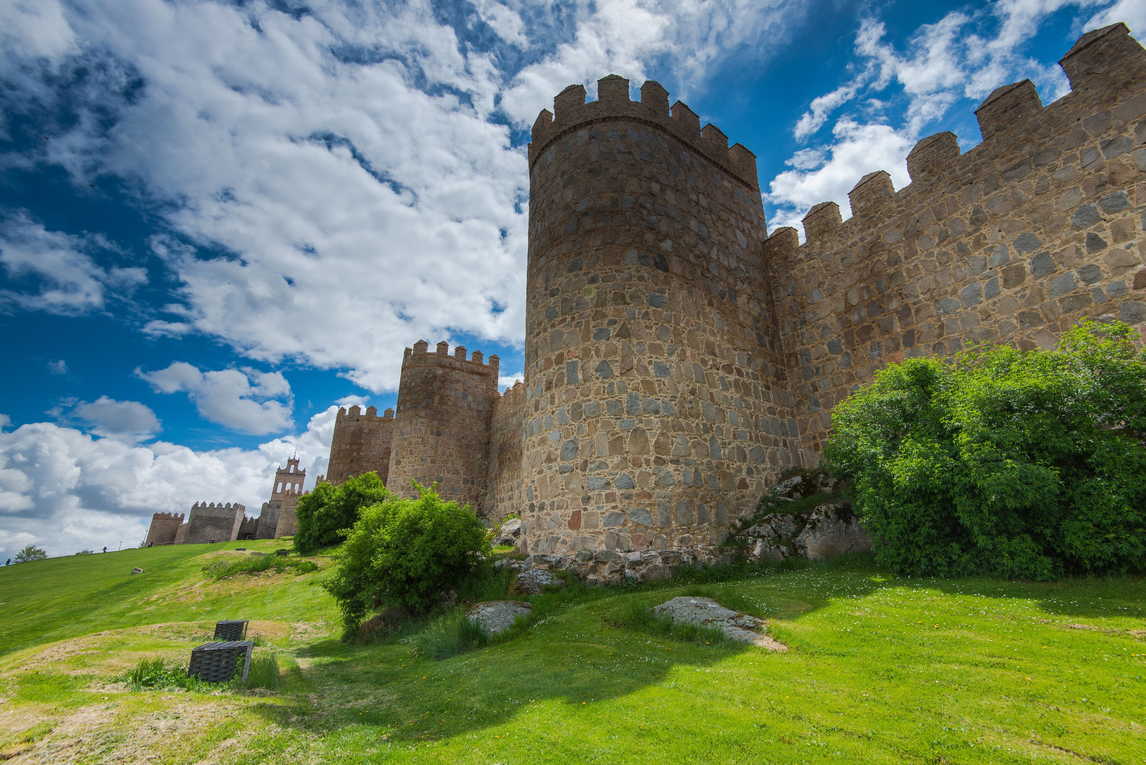 A historic stone castle with multiple towers and battlements, surrounded by lush green grass and trees.