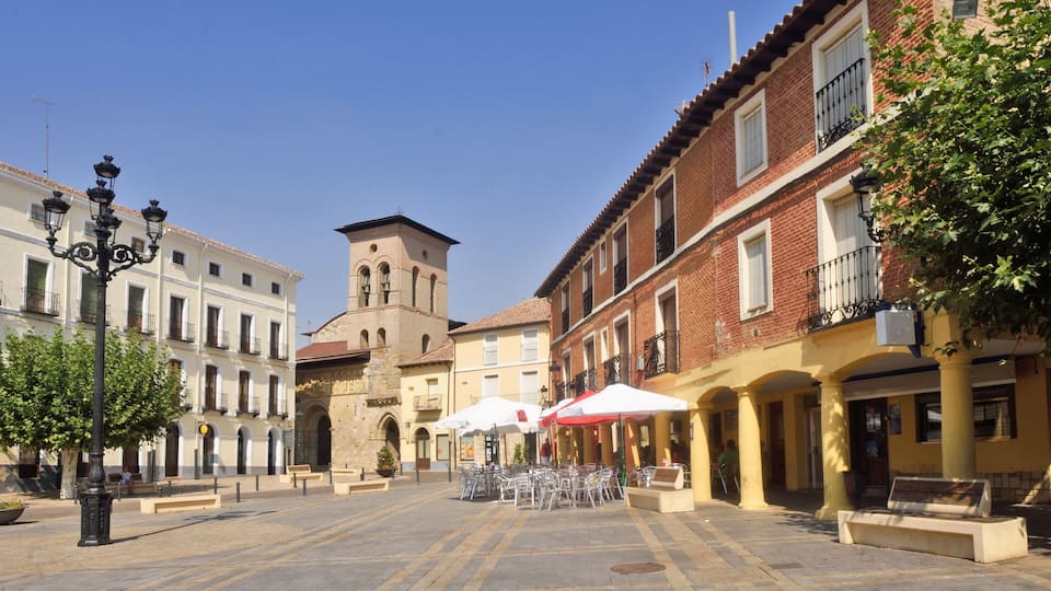 A plaza with outdoor seating, a church tower, and traditional buildings.