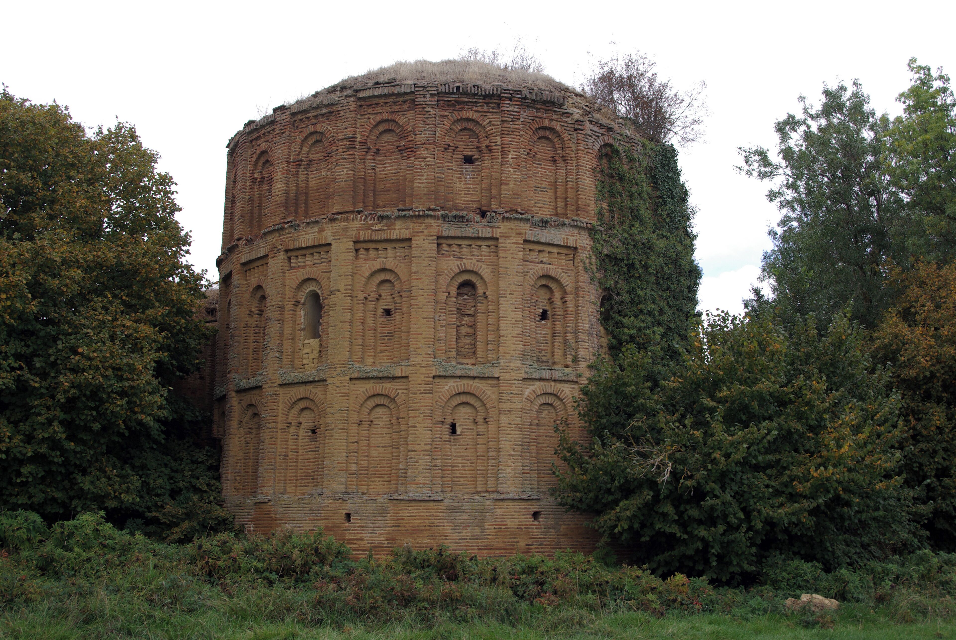 A large, cylindrical brick structure surrounded by dense foliage.